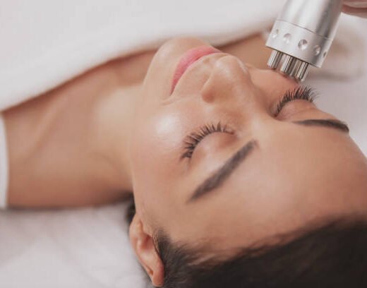 istockphoto-1164183494-612x612 Top view close up of a beautiful happy woman getting microcurrent facial treatment at beauty clinic. Attractive female patient enjoying skincare procedures by professional cosmetologist
