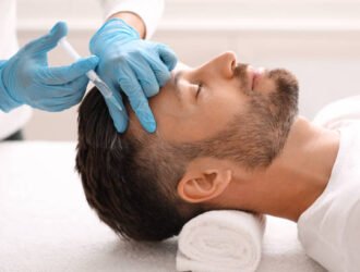 Side view of handsome middle aged man getting hair treatment at beauty salon. Man having mesotherapy session at aesthetic clinic, therapist hands in gloves making injection in scalp, closeup