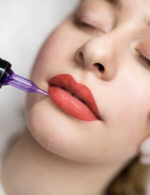 Lip Blushing. Cosmetologist applying permanent make up on lips of beautiful woman, closeup of attractive young female getting pmu treatment in beauty studio, artist using tattoo pen machine