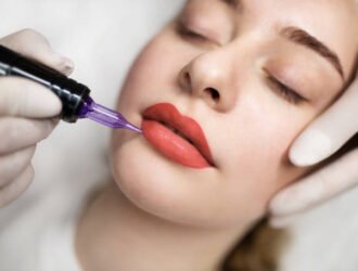 Lip Blushing. Cosmetologist applying permanent make up on lips of beautiful woman, closeup of attractive young female getting pmu treatment in beauty studio, artist using tattoo pen machine